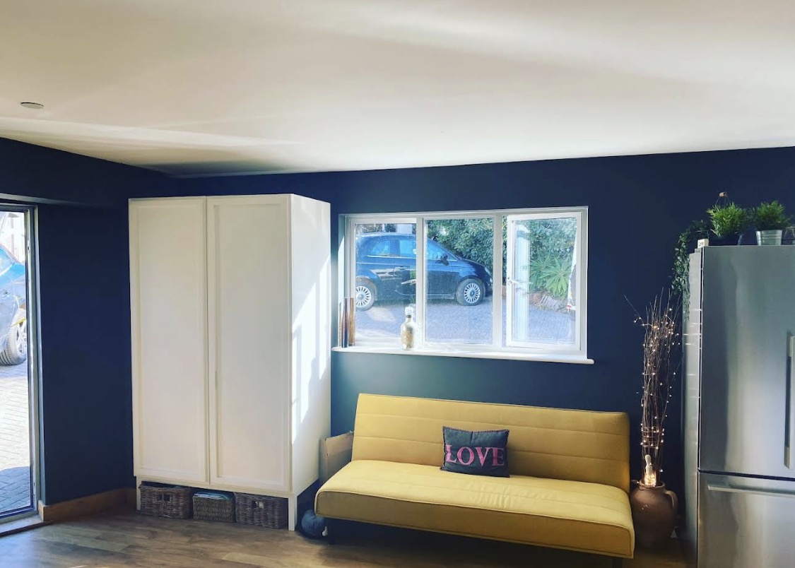 Navy living-room wall with yellow sofa and white cupboard