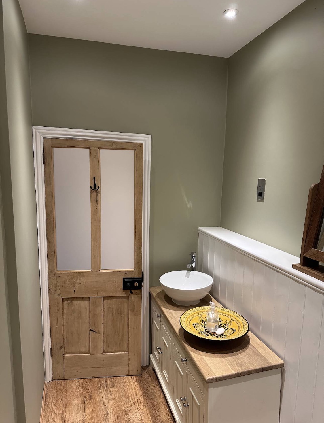 Sage cloakroom with white panelling and wooden door