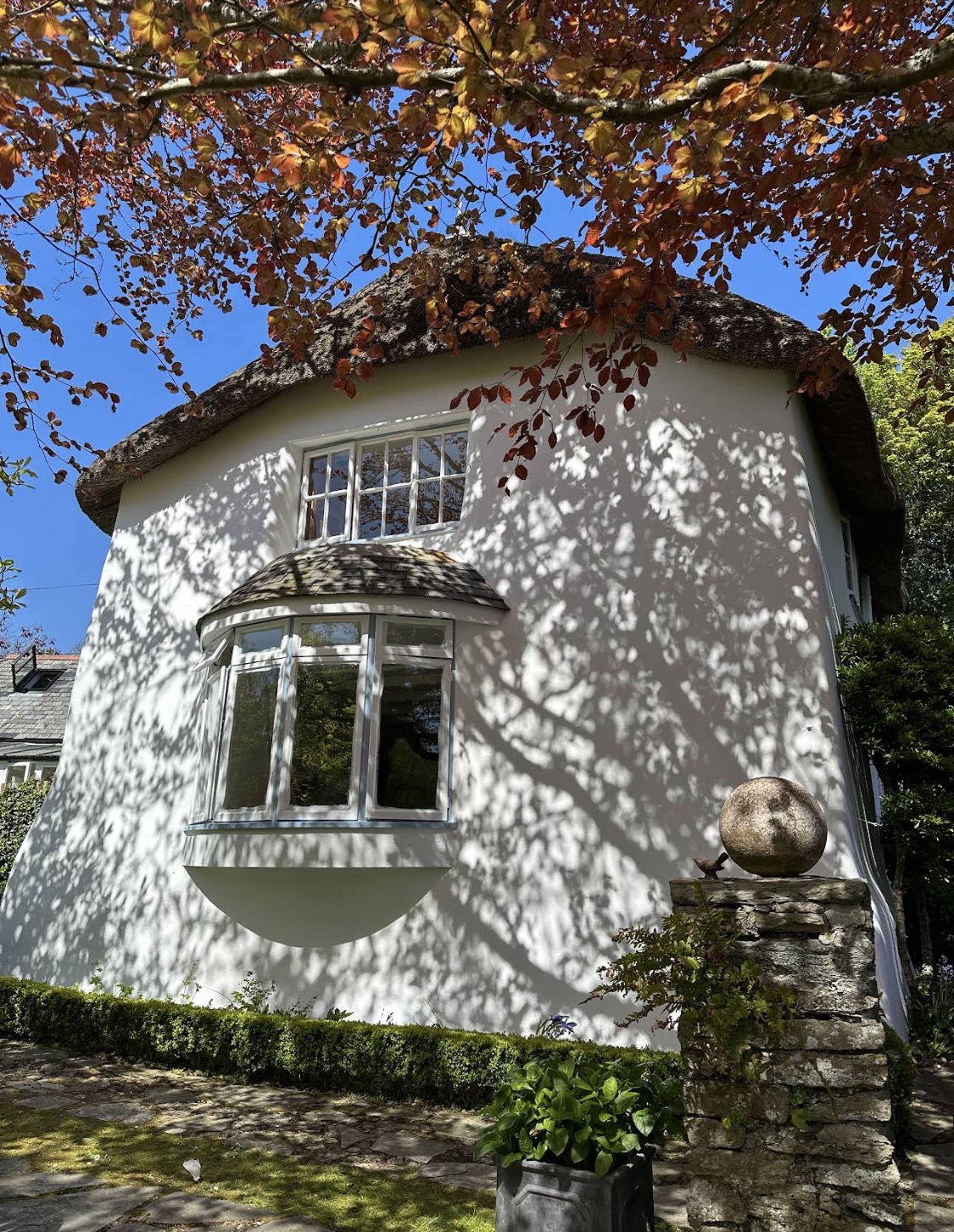 White thatched cottage with bay window beneath trees