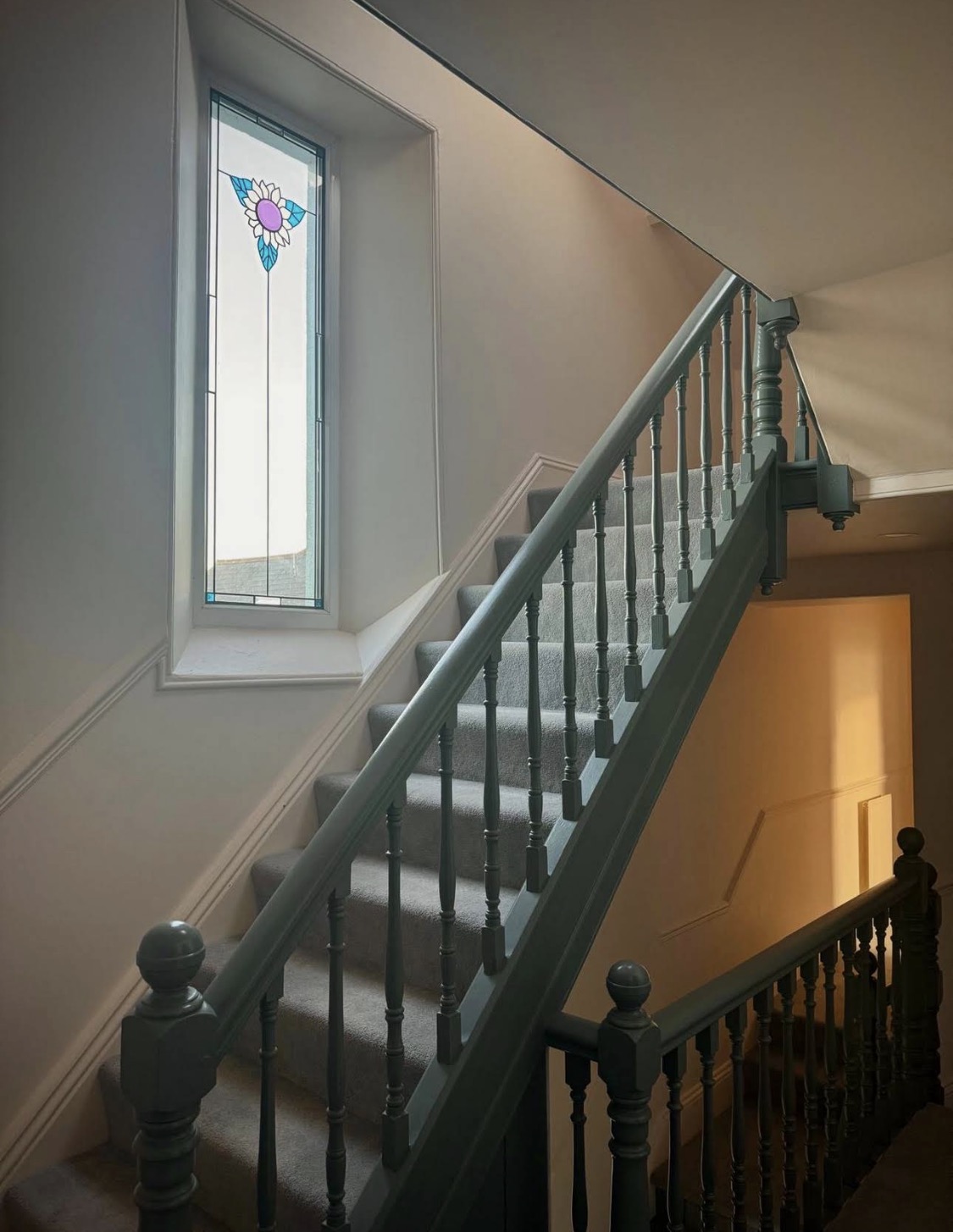 Teal painted staircase beneath a stained-glass window