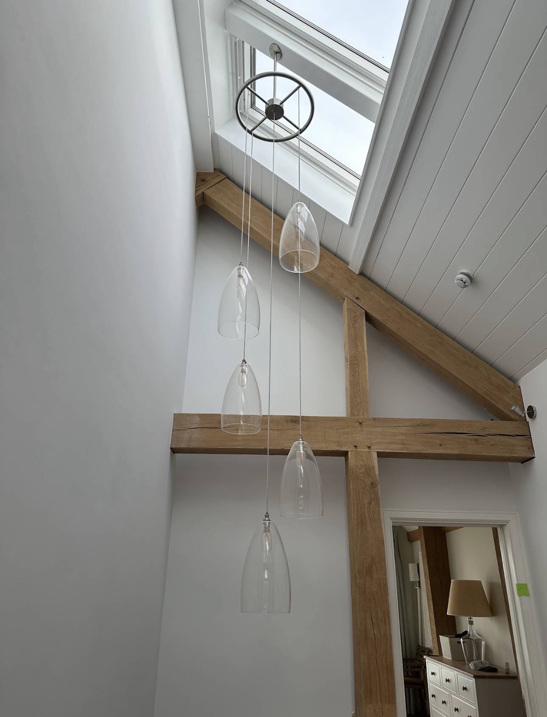Double-height white interior with oak beams and glass pendants